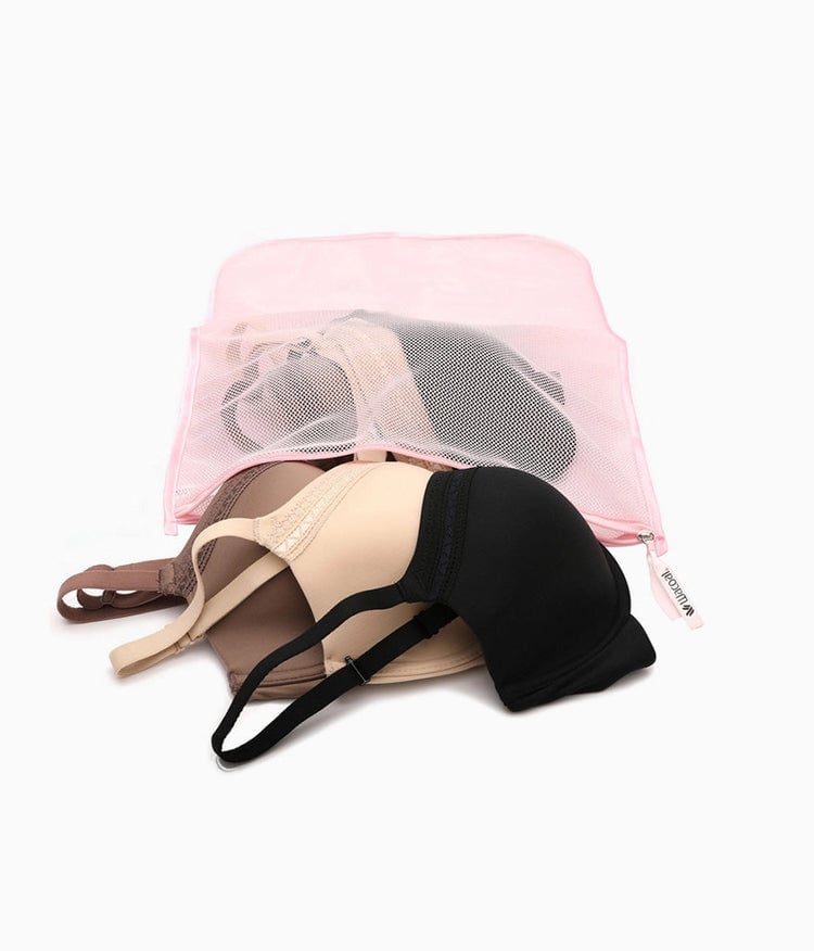 Pink mesh laundry bag containing beige, cream, and black bras on white background